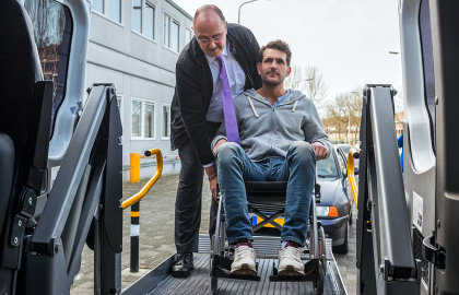 man in suit helping man in wheelchair board the vehicle