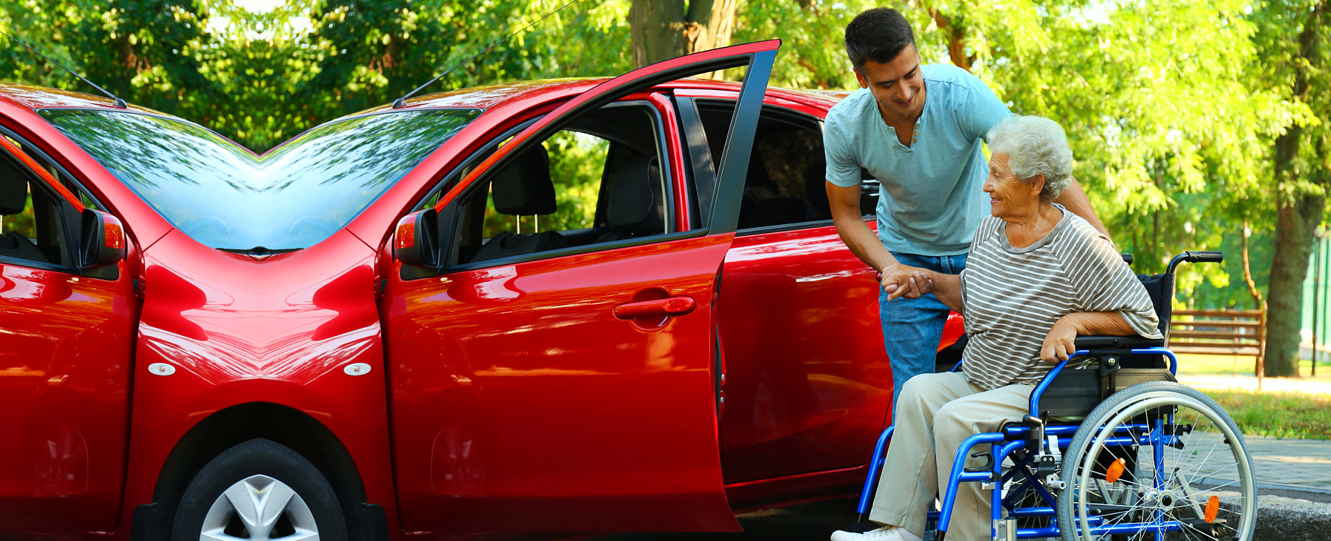 aide assisting elderly in wheelchair with boarding the red car