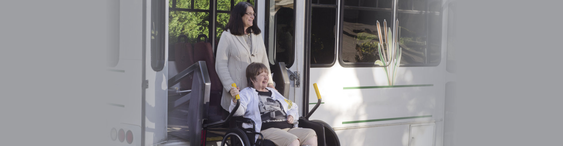 A woman in a wheelchair is helped off a van using a chair lift